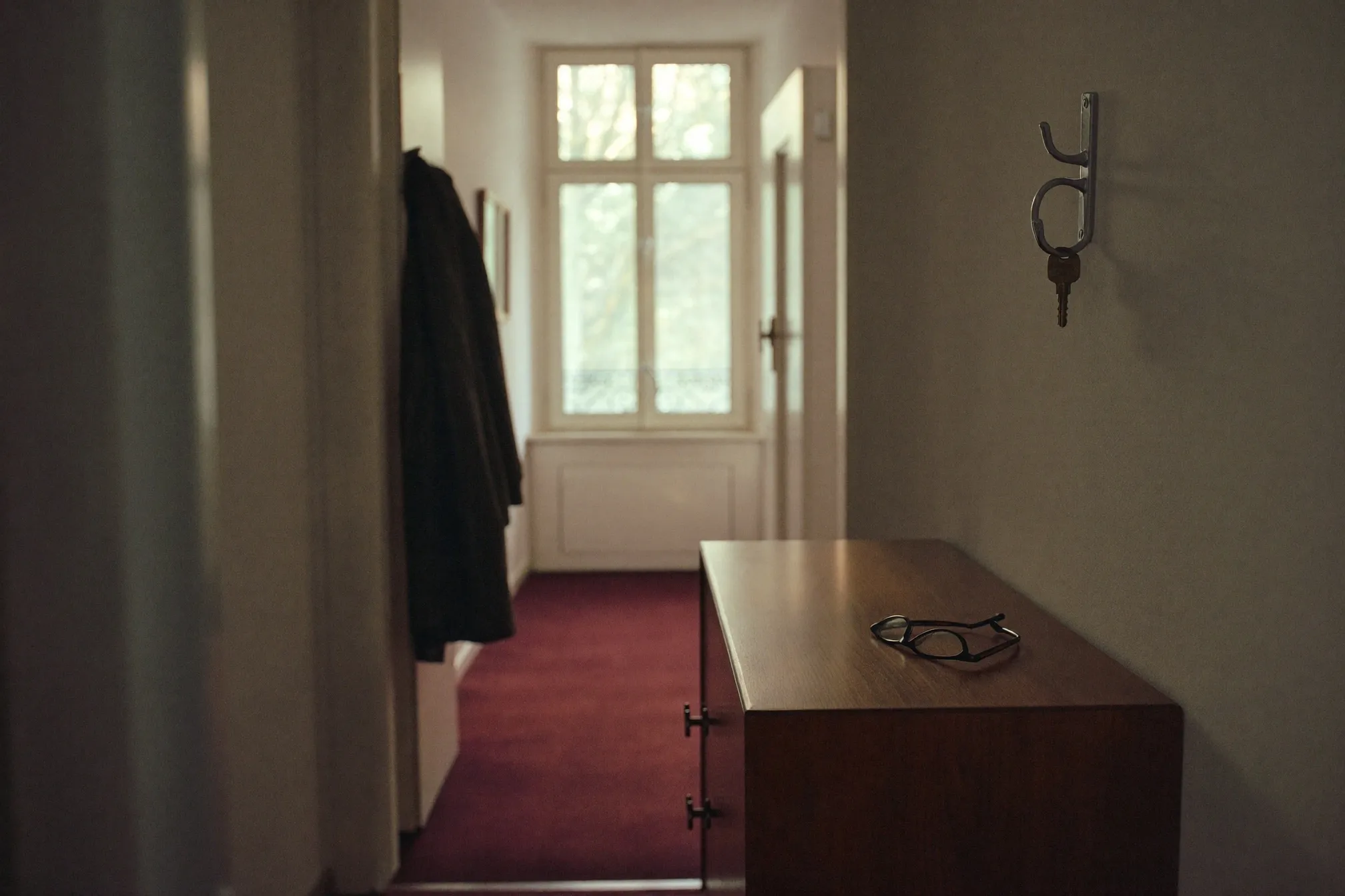 Stiller Wohnungsflur mit einer Lesebrille auf der Kommode und einem Schlüssel am Wandhaken.